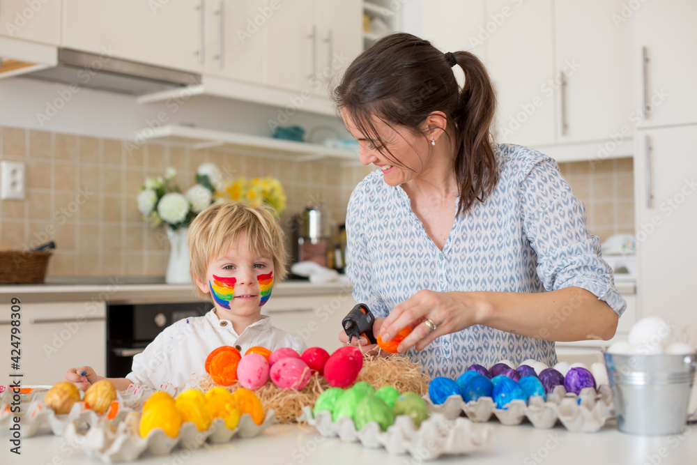 Beautiful blond child, toddler boy, painting easter eggs with mother at home, making easter wreath Beautiful blond child, toddler boy, painting easter eggs with mother at home, making easter wreath