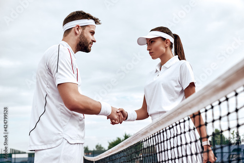 Handsome man and beautiful woman are shaking their hands while playing tennis on tennis court outdoors © Friends Stock