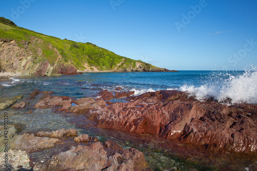 Beautiful red rocks Talland Bay Cornwall England UK with blue sea and waves