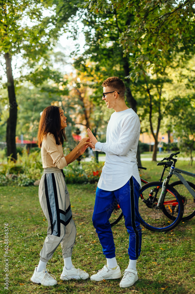 Obraz premium Vertical photo of a funny playful couple messing around in the city park, having fun, laughing, enjoying their leisure. Carefree boyfriend and girlfriend are smiling.