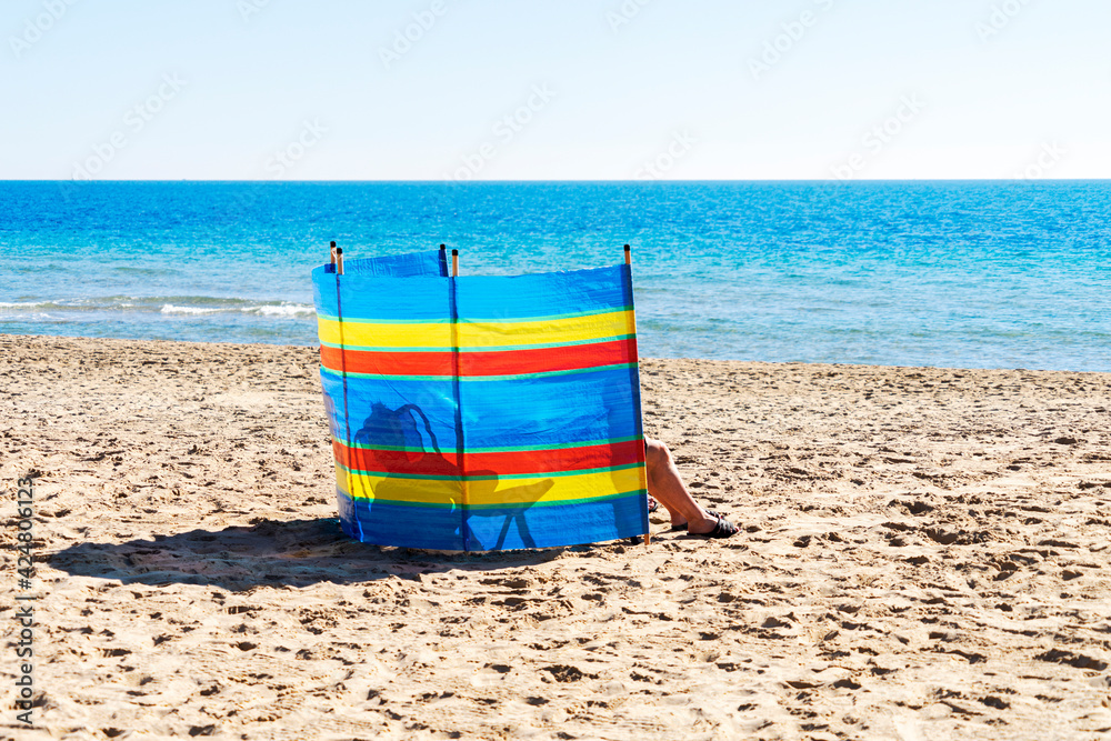 Two people relaxing behind colorful striped windscreen on the beach near the sea