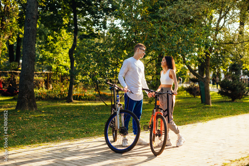 Two people, male and female are having a date in the city park and riding their colorful bicycles. Young stylish couple is holding hands and smiling.