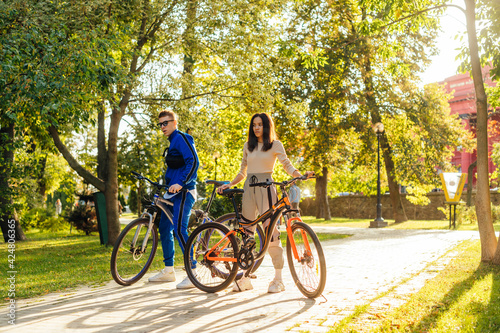 Concentrated couple of young cyclists is riding bicycles in the city park on a sunny summer day. Man and woman in colorful casual attire.