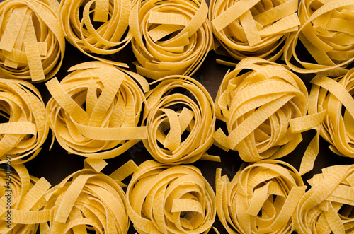 Fettuccine Tagliatelle pasta on grey background. Spaghetti nests. Yellow pasta.Uncooked ingredient for traditional Italian cuisine.Top view
