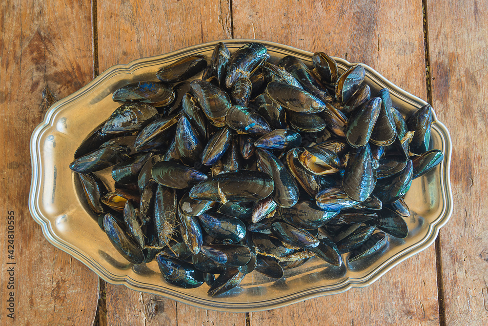 Beautiful plate of metal with heap of cooked mussels on old non paitn wooden background top view Beautiful plate of metal with heap of cooked mussels on old non paitn wooden background top view