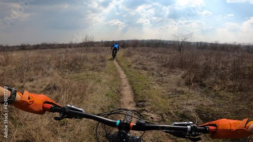 Two cyclists are riding the trail across the field. From the first person.