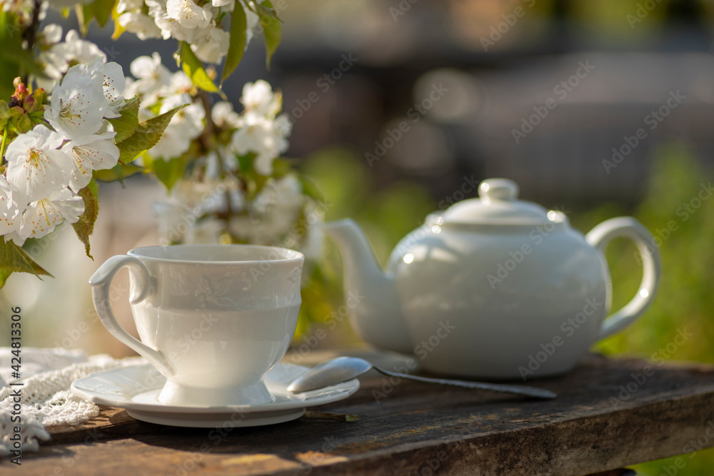 Fototapeta premium Elegant cup, tea pot, cherry blossom branches, wooden table. Outdoor breakfast, picnic, brunch, spring mood. Soft focus
