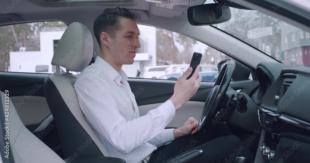 Young businessman having video chat using smartphone while sitting in a car. Male driver talking video call on mobile phone. Young businessman having video chat using smartphone while sitting in a car. Male driver talking video call on mobile phone.