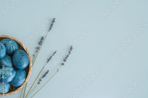 Stylish Easter composition with blue Easter eggs in a basket and a bouquet of lavender on a gentle blue background. Copy space, top view, flat lay. Easter concept