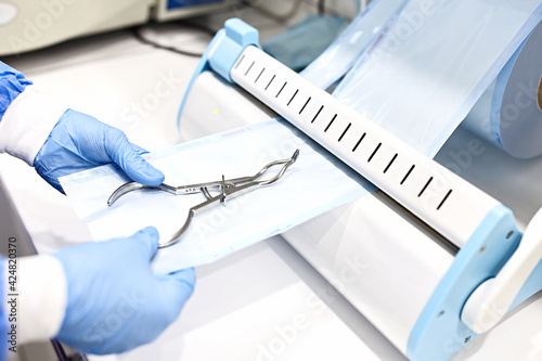 Sterilizing medical instruments in autoclave. Dental office. Close up dentist assistant's hands holding packaged with vacuum packing machine medical instruments ready for sterilizing in autoclave.