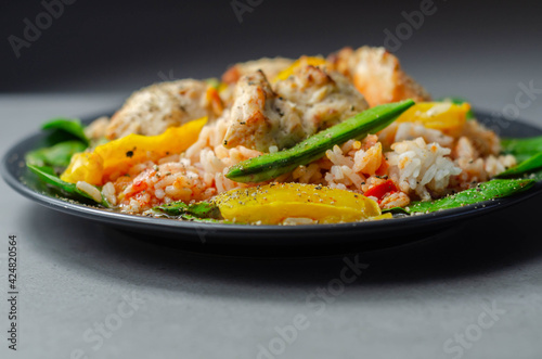 Cooked chicken breast pieces with peppers, sugar snap peas, and baby leaf spinach in a spicy sweet and sour sauce with fragrant rice