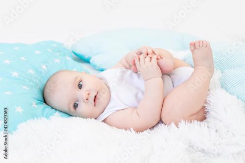 baby boy in the crib before going to bed with blue textiles playing with his feet, cute six-month-old baby