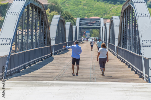 View of a senior couple of tourists on backs, strolling through the metallic bridge of the city of Peso Regua
