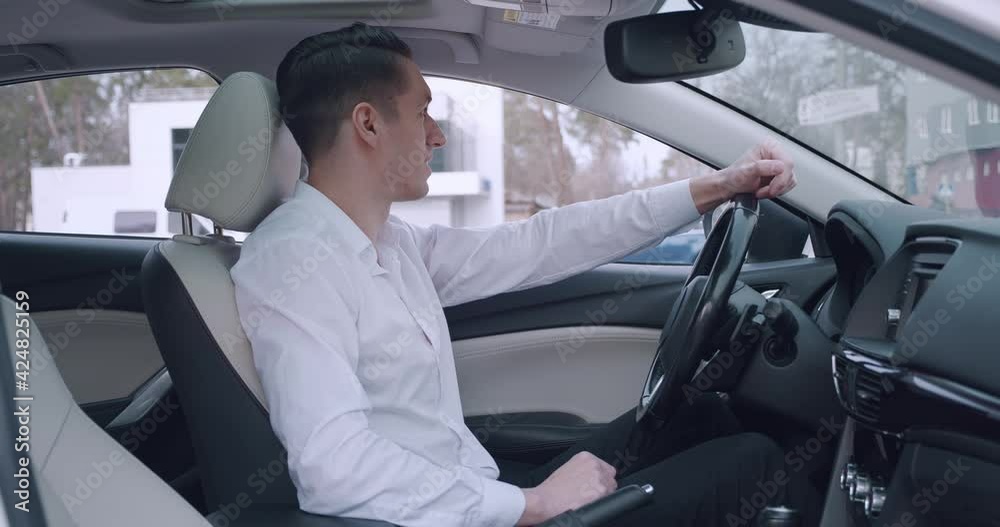 Portrait of young smiling man businessman in white shirt sitting in the car. Handsome male driver looks at the camera and smiles. Portrait of young smiling man businessman in white shirt sitting in the car. Handsome male driver looks at the camera and smiles.