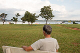 Senior man at Parque Das Garças, in Brasilia, sitting on a bench enjoying himself looking over Lake Paranoa
