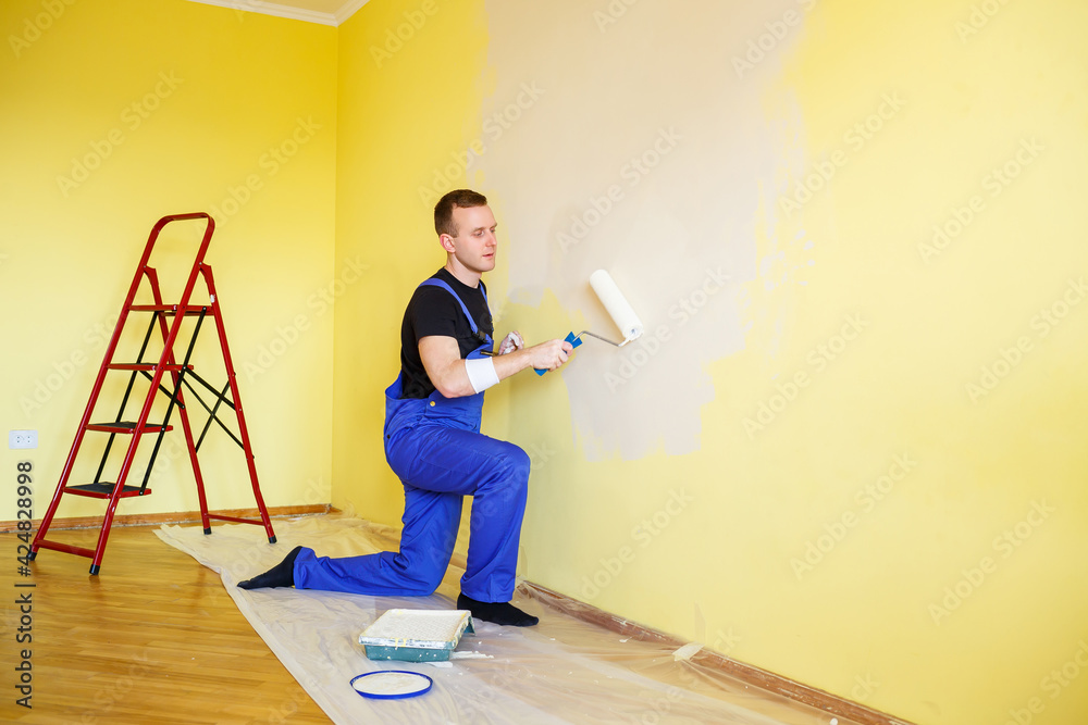 A man paints the wall in the house with a roller and paint. Renovation of rooms in the house.