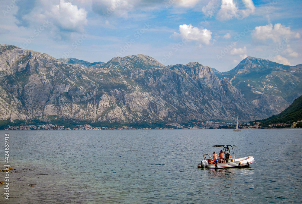 Bay of Kotor on a sunny evening with two unrecognizable men in an inflatable motor boat. Mountains and sea. Beautiful nature. Bay of Kotor on a sunny evening with two unrecognizable men in an inflatable motor boat. Mountains and sea. Beautiful nature.