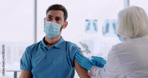 Old female doctor making vaccine injection for young customer in the laboratory clinic during lockdown. Quarantine coronavirus. Vaccination.