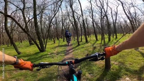 A column of cyclists rides along a forest path. First-person view.
