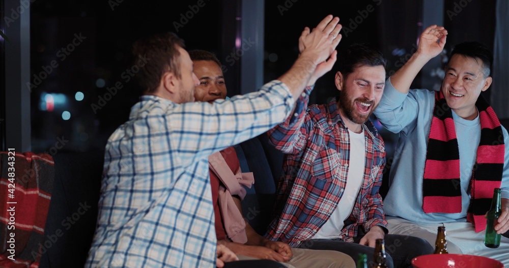 Fototapeta premium Group of funny male friends multi-ethnic men football fans gathering at night together watching soccer gameplay competition match on TV.