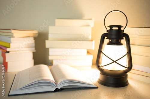 Kerosene lamp lit on a table with stacked books and an open book. Knowledge concept.