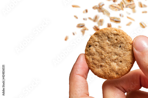 Pessoa segurando um biscoito integral com flocos de aveia caindo e fundo branco. Vetor com espaço para texto.