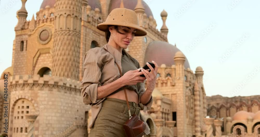 beautiful girl in travel hat, safari clothing makes a selfie on a mobile phone, India, against the background of the temple.a traveler is resting after exploring the cultural attractions of india. beautiful girl in travel hat, safari clothing makes a selfie on a mobile phone, India, against the background of the temple.a traveler is resting after exploring the cultural attractions of india.