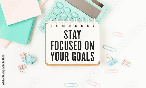 Inspirational quote - Stay focused on your goals. With text message on white paper book, pen, a cup of morning coffee, flower.