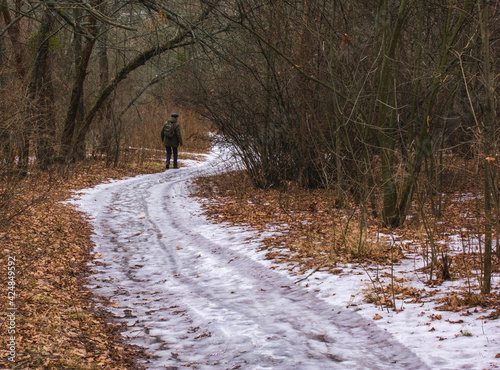 lonely man with a backpack going away through the snow covered road into the thick winter forest