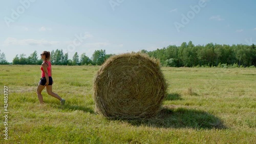 Wallpaper Mural An elegant girl in the summer in the field tries to jump on a haystack. A beautiful girl on a sunny day in shorts, a red T-shirt and glasses tries to climb a haystack, but fails Torontodigital.ca