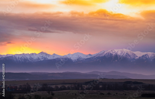 Dramatic early sunrise landscape over carpathian mountains range covered in snow with beautiful orange sky and clouds