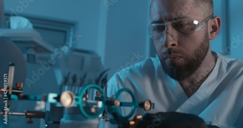 A male medical worker wearing black latex gloves and disposable eyeglasses is checking a detail on the axiosplit device and inside of it is the human ceramic model of a jaw.