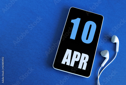 April 10. 10 st day of the month, calendar date. Smartphone and white headphones on a blue background. Place for your text. Springtime month, day of the year concept