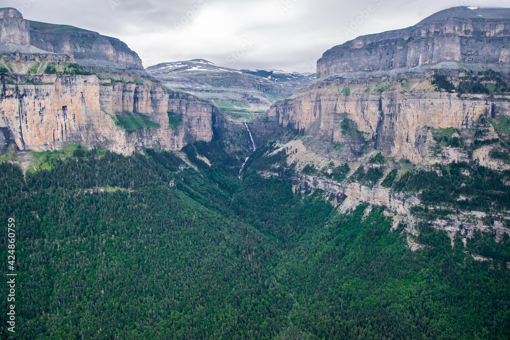 El bosque mixto de coníferas y hayas asciende por las laderas de roca caliza del valle glaciar, al tiempo que desciende una estrecha cascada en el Parque Nacional de Ordesa, en los Pirineos españoles