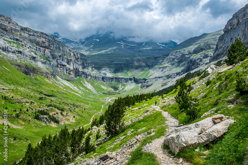 Un camino de alta monta  a recorre la ladera de un valle glaciar en direcci  n al circo atravesando praderas y pinos bajo un cielo que amenaza tormenta en el Parque Nacional de Ordesa  en los Pirineos e