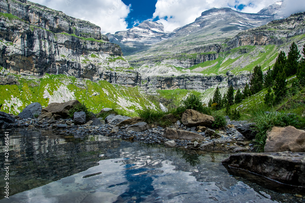 El circo glaciar del valle de Ordesa se refleja en un pequeño estanque natural formado por los múltiples arroyos del deshielo a principios del verano en el Parque Nacional de Ordesa, Pirineos españole