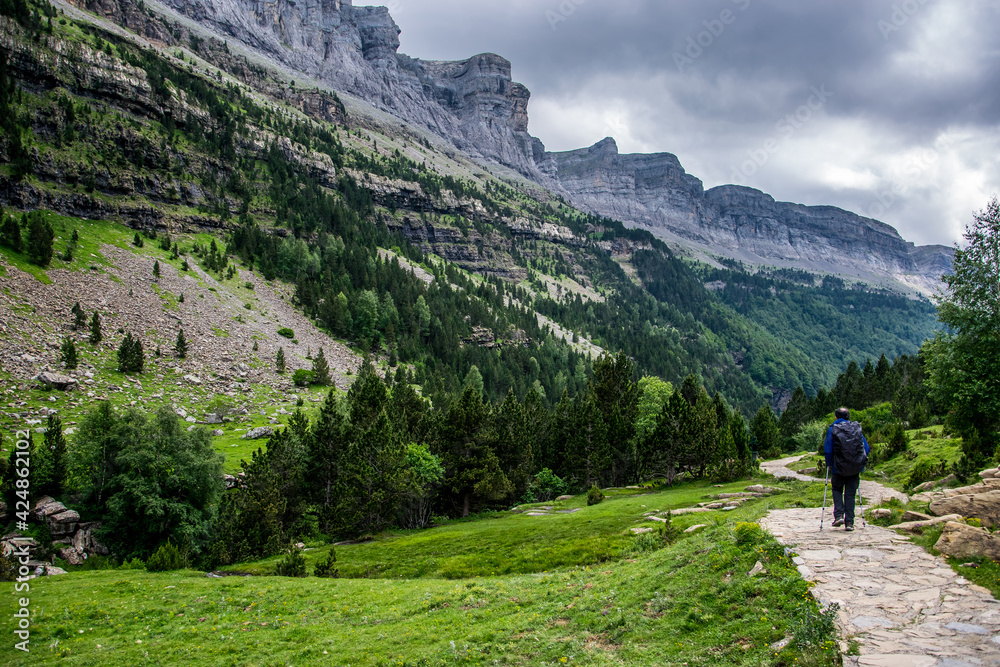 Un deportista camina por un sendero junto al río Arazas con los bosques mixtos de coníferas y hayas, y las paredes rocosas del valle glaciar del Parque Nacional de Ordesa, en los Pirineos españoles