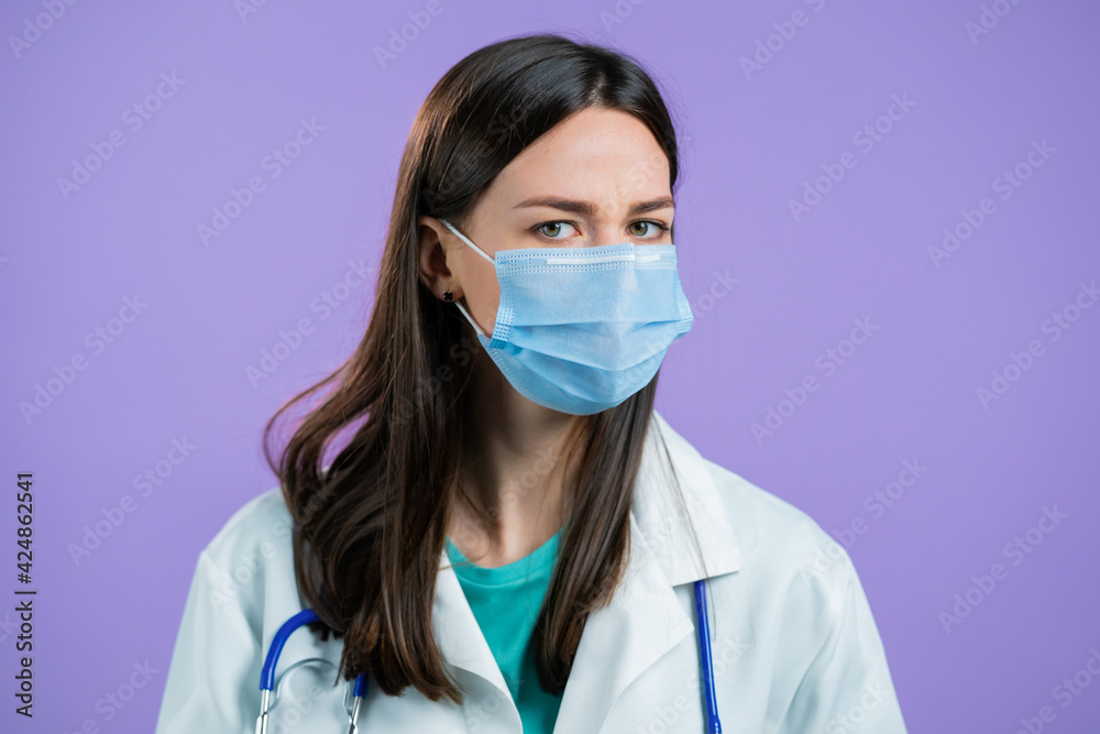 Portrait of nurse in protective medical mask and coat disapproving with no head gesture. Denying, Rejecting, Disagree, Portrait of female doctor on violet background Portrait of nurse in protective medical mask and coat disapproving with no head gesture. Denying, Rejecting, Disagree, Portrait of female doctor on violet background