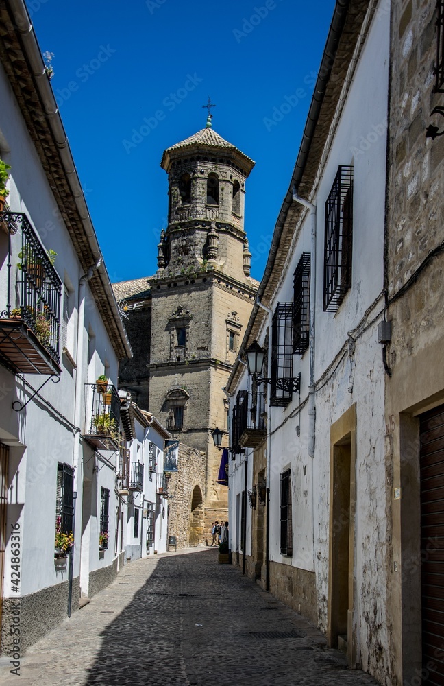 Torre de una iglesia al final de una calle estrecha de casas encaladas en el casco antiguo de Baeza, España, perteneciente a la lista del Patrimonio Mundial de la UNESCO