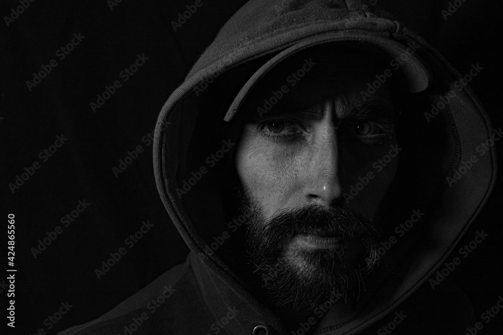 face of a man in shadows with cap and hood on a black background
face of a man in shadows with cap and hood on a black background