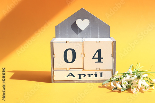 Calendar for April 4: cubes with the numbers 0 and 4, the name of the month of April in English, a bouquet of blooming snowdrops on a yellow background in the sun and in the shade of objects photo