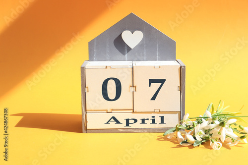 Calendar for April 7: cubes with the numbers 0 and 7, the name of the month of April in English, a bouquet of blooming snowdrops on a yellow background in the sun and in the shade of objects photo