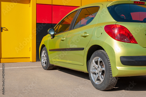 Part of a family green car parked in front of the modern house or garage yellow door. Back view. Repair station concept. Place for text on the door.