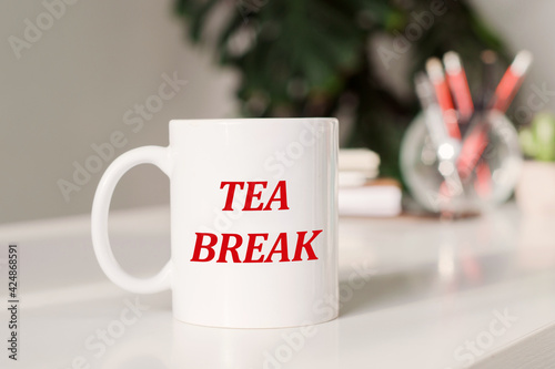 Coffee mug with text - TEA BREAK in workplace background.