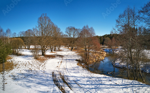 Obraz na płótnie Early spring landscape with melting snow. Dirt rural road, wood, ice and snow panorama. w salonie