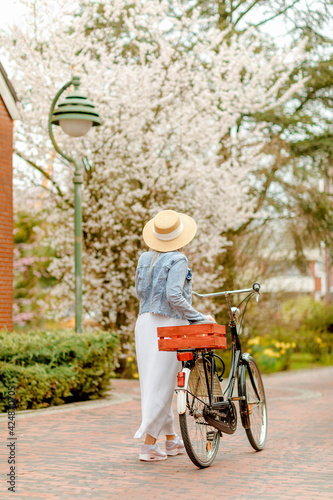 Fototapeta Naklejka Na Ścianę i Meble -  Woman with bike and a blossoming tree in the background. Sympathetic woman walks in the city center with her bike. Bicycle rails in the pedestrian zone. European city. Spring mood.	