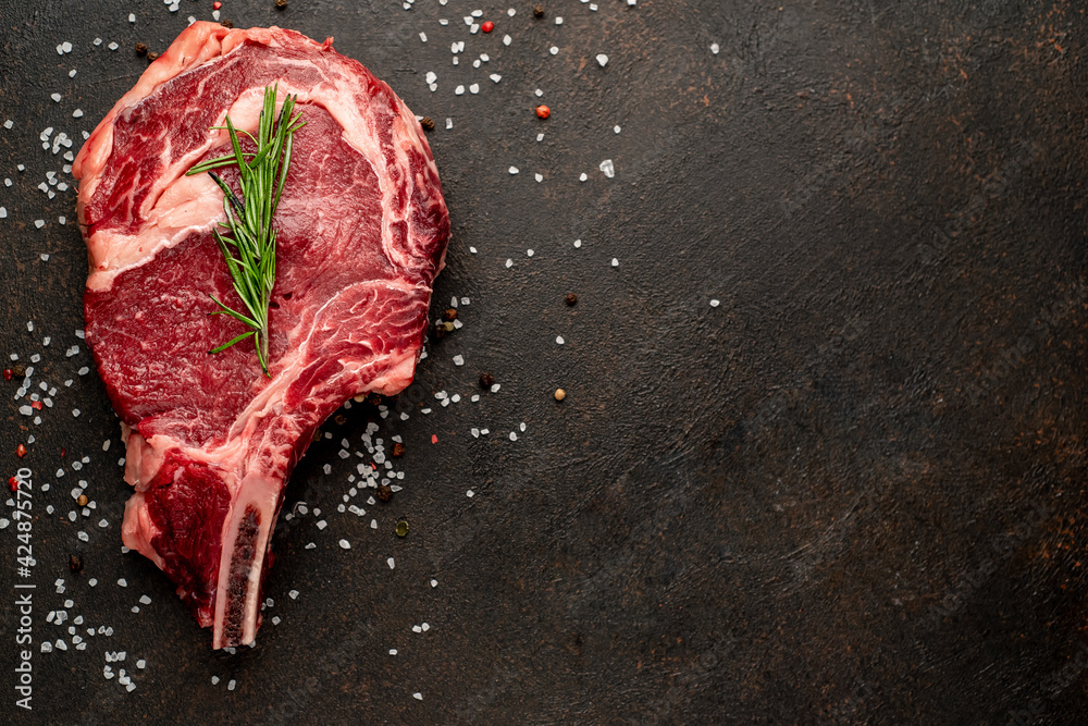 raw ribeye steak with spices on stone background with copy space for your text