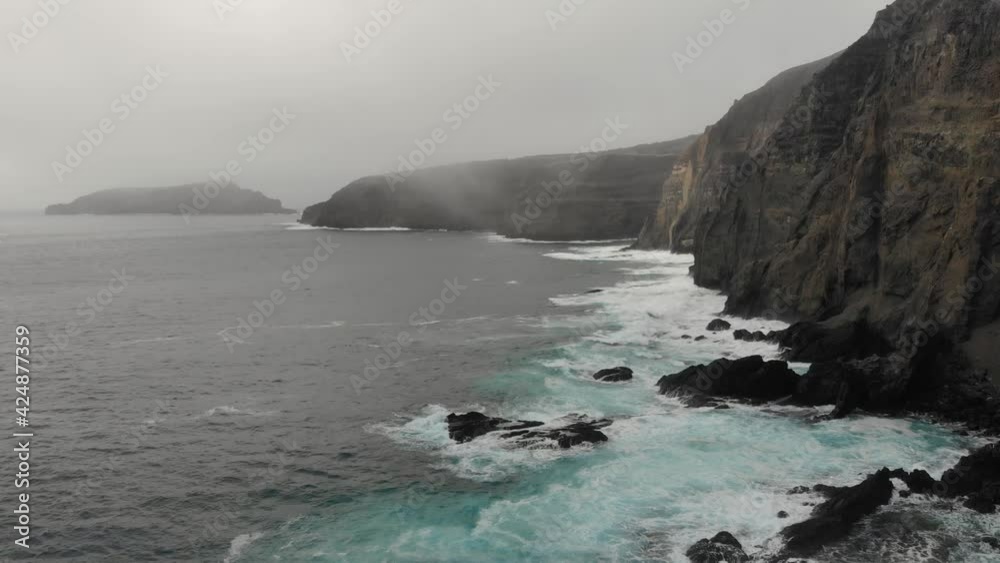 Ocean waves slamming rocks at Ponta da Calheta on Porto Santo island. Aerial backward