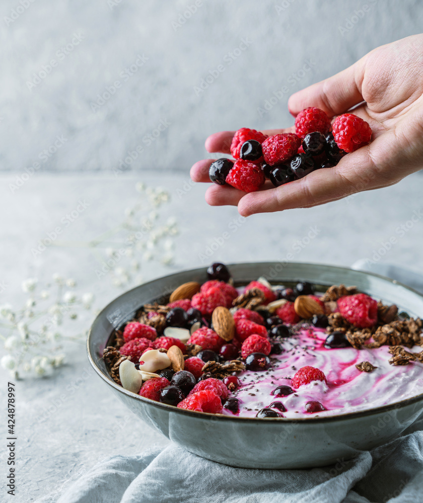 Hand throws berries in bowl with yogurt, granola, muesli, seeds, frozen  raspberries, nuts on light background. Healthy food, detox smoothy,  vegetarian nutrition, close up Stock-Foto | Adobe Stock