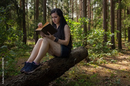 Girl sitting on a fallen tree in the forest and reading a book